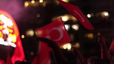 Karanlık bir gökyüzüne karşı Türk bayrağını ağır çekimde tutan ve sallayan bir kişi, ulusal gurur ve kutlamaları vurguluyor