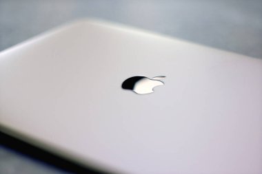 İzmir, Türkiye - 11 Eylül 2024: Apple MacBook dizüstü bilgisayarının sığ bir alan derinliğine sahip, Apple logosuna odaklanmış, bulanık, atmosferik bir arkaplan yaratıyor