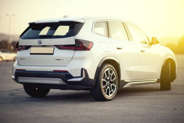 İzmir, Türkiye - 11 Kasım 2024: Gün batımında çekilen ve zarif tasarımını sıcak altın ışıkta sergileyen inci beyazı BMW IX1 e-sürücü elektrikli SUV 'nin üç çeyrek görünümü.