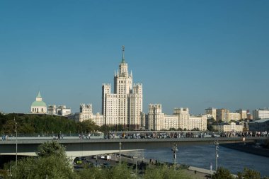 Moskova, Rusya - 15 Ağustos 2024: Moskova Devlet Üniversitesi 'nin ağaçlardan oluşan bir tepe örtüsü altında çekilen ve açık mavi gökyüzüne karşı yükselen mimarisini gözler önüne seren manzarası.