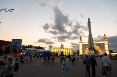 Moskova, Rusya - 17 Ağustos 2024: VDNH sergi merkezindeki Sovyet döneminden kalma bir roket ve uçağın akşam fotoğrafı, gün batımında renkli bir gökyüzü altındaki insanlarla çevrili