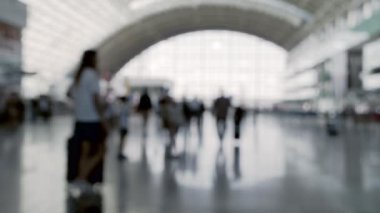 Modern bir havaalanı terminalinde bavullu yolcuları gösteren bulanık bir görüntü. Siluetler ve yumuşak odak bir hareket ve seyahat hissi uyandırıyor.