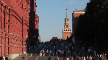 Moskova, Rusya - 16 Ağustos 2024: Kızıl Meydan 'daki Kremlin duvarındaki ikonik saati ile Spasskaya Kulesi' nin parlak güneşin altında gezen ziyaretçilerinin videosu
