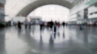 Modern bir havaalanı terminalinde bavullu yolcuları gösteren bulanık bir görüntü. Siluetler ve yumuşak odak bir hareket ve seyahat hissi uyandırıyor.