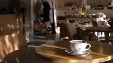 Güneşli bir kafe masasında dinlenen kahve fincanının sakin bir videosu samimi ve davetkar bir ortam yaratıyor. Kahve meraklıları ve sakin titreşimler için mükemmel.