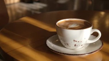 Güneşli bir kafe masasında dinlenen kahve fincanının sakin bir videosu samimi ve davetkar bir ortam yaratıyor. Kahve meraklıları ve sakin titreşimler için mükemmel.