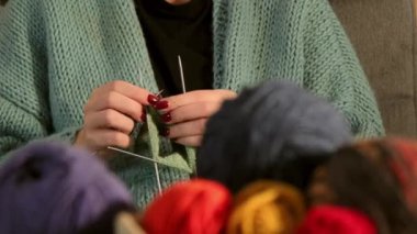 Yakından çekilmiş bir videoda genç bir kadının elleri yeşil iplikle dikkatlice örgü örüyor. Detaylı olarak vurgulanmış rahatlatıcı bir zanaat ve yaratıcılık anı