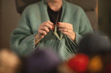 Genç bir kadının ellerinin, birden fazla iğne kullanarak yeşil iplikle dikkatlice örüldüğü detaylı bir manzara. Yaratıcılığın samimi, odaklanmış anı yakından yaklaştı.