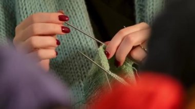 Yakından çekilmiş bir videoda genç bir kadının elleri yeşil iplikle dikkatlice örgü örüyor. Detaylı olarak vurgulanmış rahatlatıcı bir zanaat ve yaratıcılık anı