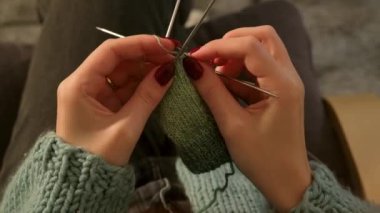 Yakından çekilmiş bir videoda genç bir kadının elleri yeşil iplikle dikkatlice örgü örüyor. Detaylı olarak vurgulanmış rahatlatıcı bir zanaat ve yaratıcılık anı