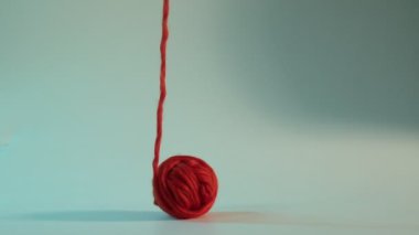 Biri ipliği yukarı doğru çekerken, turuncu iplik topu zıplar ve ağır çekimde takla atar. Düz beyaz bir zemine doğru, dinamik ve oyuncu hareketler yaratır.