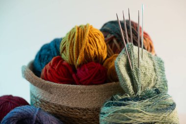 Bir sepete düzgünce dizilmiş renkli iplikler, örgü iğneleriyle birlikte, temiz beyaz bir arka plan üzerine kurulmuş, yaratıcılık ve sanatsal tutku sergiliyor.