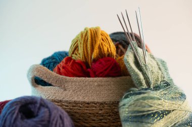 Bir sepete düzgünce dizilmiş renkli iplikler, örgü iğneleriyle birlikte, temiz beyaz bir arka plan üzerine kurulmuş, yaratıcılık ve sanatsal tutku sergiliyor.
