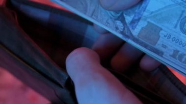 Birkaç yüz dolarlık banknotların boş bir cüzdana konduğu, zenginliği, mali yönetimi ve tasarruf ve para yönetimi kavramını temsil eden yakın plan bir video.