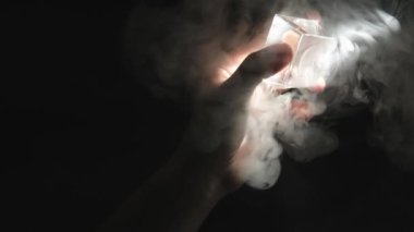 Dumanlı bir atmosferdeki bir ışık demetine doğru şeffaf bir cam nesneyi tutan bir erkeğin yavaş çekimde yakın plan çekimi.