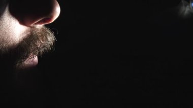 Elektronik bir sigaradan buhar soluyan bir adamın, dramatik ışıklandırma ve gizemli dumanlı atmosferle sade bir ortamda yakalandığı yakın çekim yavaş çekim videosu.