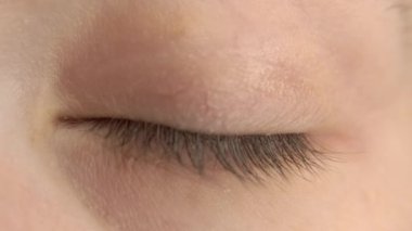 Bir kadının kapalı gözünün yavaşça açıldığı, kirpiklerini, göz kapaklarını ve ince deri dokularını doğal ve samimi bir perspektifte gösteren yakın plan bir video.