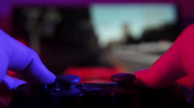 Yarış video oyunu oynarken elinde oyun kumandası olan bir adamın yakın çekim görüntüsü. Arka planda bir araba yarışını gösteren bulanık bir TV ekranı var