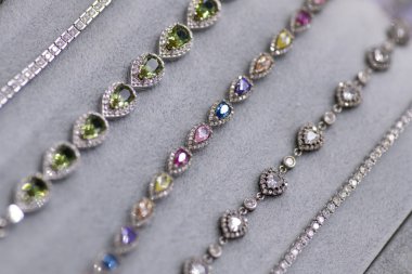 A detailed close-up of luxurious gemstone necklaces and anklets, featuring vibrant, sparkling stones set in silver and gold, displayed on a soft gray background for an elegant presentation clipart