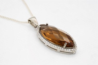 Parlak beyaz elmaslarla çevrili gümüş bir kolyeye yerleştirilmiş, büyük, yüzlü kahverengi bir taş içeren çarpıcı bir kolyenin yakın çekimi.