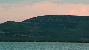Flamingoların nefes kesici yavaş çekim videosu canlı bir günbatımı gökyüzünde zarifçe uçarak barışı ve doğal güzelliği çağrıştırıyor.