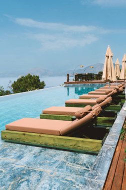 Bir otelin yaz mevsiminde güneşlenenlerle paylaştığı sonsuz havuzun gündüz fotoğrafı, lüks bir rahatlama sergileniyor..