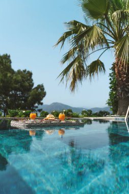 Yüzme havuzunda güzelce düzenlenmiş, taze meyve, hamur işi ve içecekler içeren savurgan bir kahvaltı..