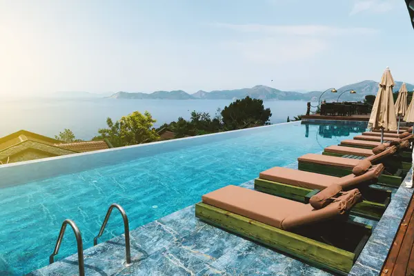 Bir otelin yaz mevsiminde güneşlenenlerle paylaştığı sonsuz havuzun gündüz fotoğrafı, lüks bir rahatlama sergileniyor..