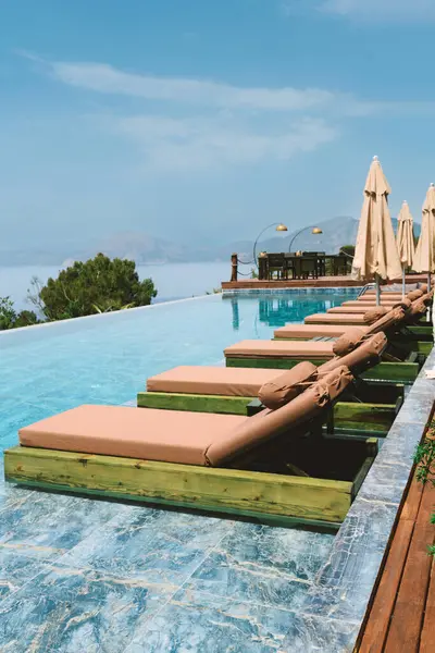 Bir otelin yaz mevsiminde güneşlenenlerle paylaştığı sonsuz havuzun gündüz fotoğrafı, lüks bir rahatlama sergileniyor..