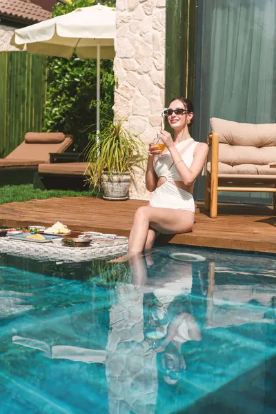 20 'li yaşlarda esmer bir kadın havuz kenarında dinlenirken suda yüzen kahvaltının tadını çıkarıyor..