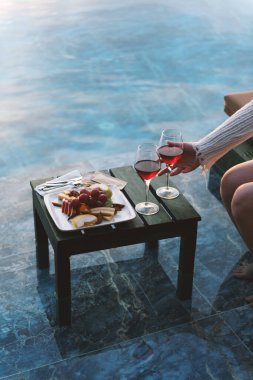 İki kırmızı şarap kadehi ve havuz kenarında güzel hazırlanmış bir meyve tabağı..