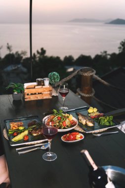 Gün batımında bir otel restoranında sunulan et, balık ve şarabın zarif bir sunumu..
