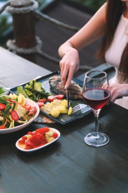 20 'li yaşlarda bir kadının, lüks bir otel restoranında balık ve patates kesmek için çatal bıçak kullanırken çekilmiş yakın plan fotoğrafı..