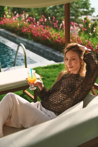 20 'li yaşlarda sarışın bir kadın otelinin özel bahçesinde poz verirken portakal suyunun tadını çıkarıyor..