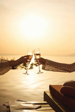 Romantik bir an, şampanya bardaklarının altın günbatımı saatinde havuz kenarında birbirine vurmasıyla çekildi..