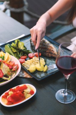 20 'li yaşlarda bir kadının, lüks bir otel restoranında balık ve patates kesmek için çatal bıçak kullanırken çekilmiş yakın plan fotoğrafı..