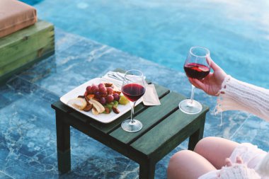 İki kırmızı şarap kadehi ve havuz kenarında güzel hazırlanmış bir meyve tabağı..