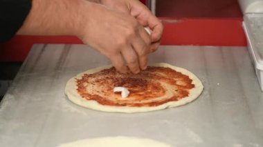 Yavaş çekimde şefin ellerine yaklaş. Profesyonel mutfakta soslu pizza hamuruna peynir parçaları koy.