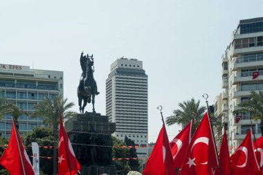 Mustafa Kemal Atatürk heykeli meydanda, önünde Türk bayrakları sallayarak milli gurur ve saygı gösteriyor. 