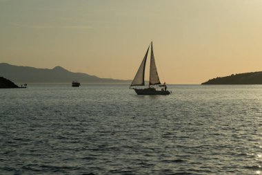 Denizde süzülen bir yelkenlinin güzel bir fotoğrafı, dingin suları yakalıyor ve parlak bir gökyüzünün altında berrak bir ufuk çiziyor.