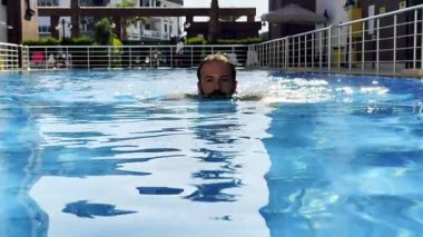 Güneşli bir öğleden sonra, sakin ve istikrarlı bir şekilde havuzda yüzen bir adamın sakin bir şekilde, sakin bir öğleden sonra yüzdüğü bir video.