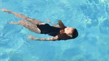Otel havuzunda siyah mayosuyla yüzen 10 yaşındaki bir kızın huzurlu ve yavaş çekim videosu.