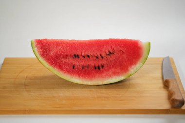 Tahta bir tahtadaki karpuz diliminin, sulu dokusunu ve canlı kırmızı rengini gözler önüne seren, beyaz bir zemine yakın plan fotoğrafı.