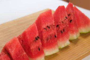 Bir karpuz diliminin yakın plan fotoğrafı, yenilebilir bir şekle bürünmüş, tahta bir tahta üzerinde beyaz bir zemin üzerinde, sulu tazeliğini vurguluyor.