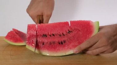 Tahta bir tahta üzerinde beyaz bir zemine karşı bıçakla kesilmiş bir karpuz dilimini gösteren bir video taze meyve hazırlığını vurguluyor.