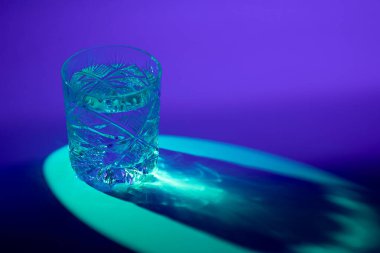 Kesik bir viski bardağının mavi noktalı arka ışıklandırmayla aydınlatılmış şekli ve ışık kırılması nedeniyle yerde yakıcı desenler oluşturan bir fotoğrafı.