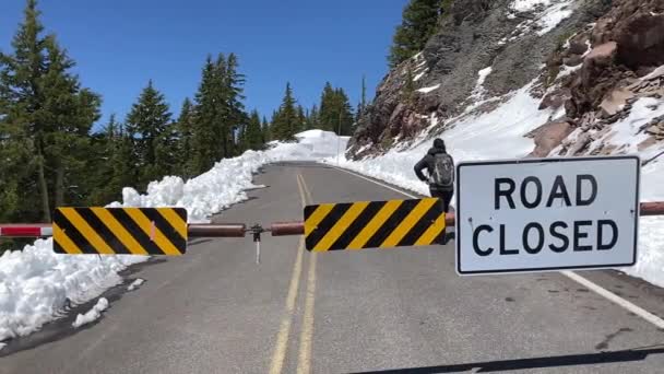 在环湖环路上 一名妇女走过封闭的路障 雪堤在路的两边 美国俄勒冈州的火山湖国家公园 — 图库视频影像