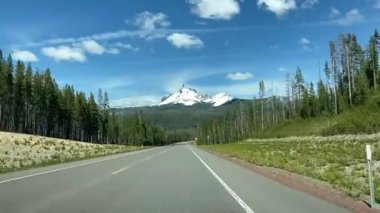 Karla kaplı Thielsen Dağı manzaralı Krater Gölü yakınlarında Oregon 'da kırsal bir yol kullanmak. Sürücülerin bakış açısı ön camdan geçer, her yer yemyeşil ormanlarla çevrilidir - Oregon, ABD