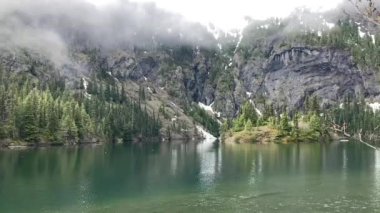 The rippling, turquoise water of Lake Angeles as low-level clouds roll into the mountains. The steep rock wall of the mountain in the background - Nr Port Angeles, Washington, USA