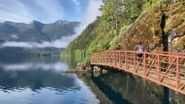 Female Hiker Crosses Red Metal Bridge Still Lake Surrounded Forest — Stock Video